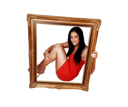 A beautiful young teenager girl sitting on the floor in a red strapless dress with her long black hair, holding a picture frame before her, over white.