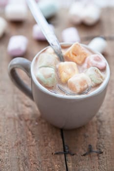 Closeup of cup of hot chocolate with spoon and coloured marshmallows resting on wooden table