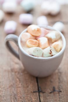 Closeup of cup of hot chocolate with coloured marshmallows resting on wooden table