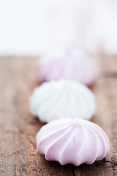 Closeup three pink and white meringues resting on wooden table