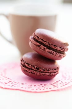 Closeup of two chocolate macaroons with cup in background