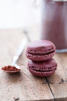 Closeup of two macaroons on wooden table with glass jar of cocoa powder and spoon