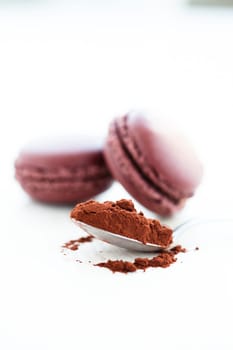 Closeup of cocoa powder in spoon with two macaroons in background