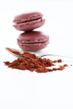 Closeup of cocoa powder and spoon with two macaroons in background