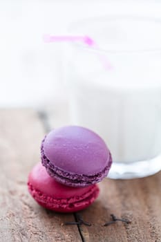 Closeup of two macaroons on wooden table with glass of milk in background