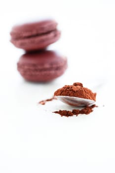 Closeup of cocoa powder in spoon with two macaroons in background