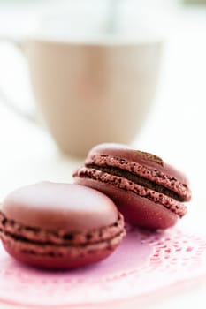 Closeup of two chocolate macaroons with cup in background