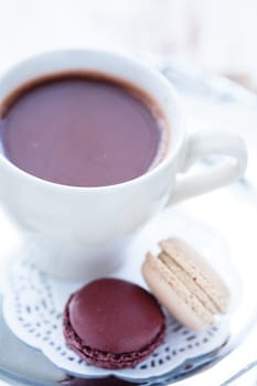Closeup of cup of hot chocolate with two macaroons on a wooden table