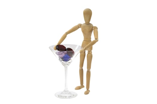 A wooden female doll is standing next to a cocktail glass