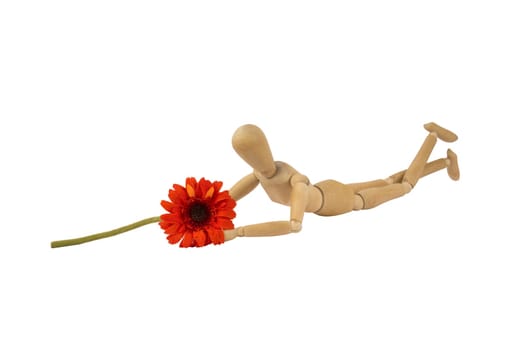 A wooden female doll is lying holding a flower