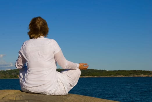 a woman in white cloth doing yoga in front of the ocean
