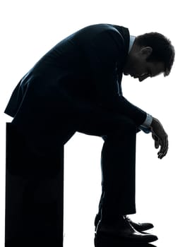 one caucasian sad business man  sitting pensive looking down  in silhouette studio isolated on white background