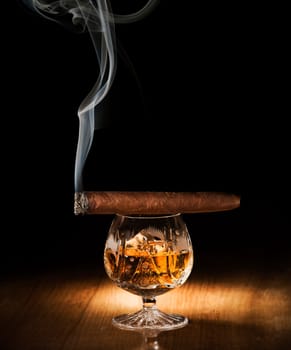 Cognac and cigar on wooden background close up