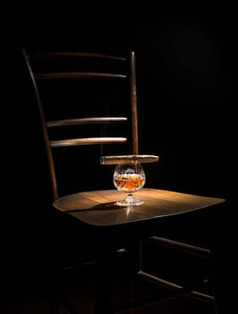 Cognac and cigar on wooden chair close up