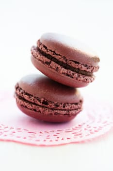Closeup of two chocolate macaroons on decorative pink mat