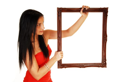 A lovely young teen girl in a red dress holding up a picture frame, in a red dress and black hair standing in the studio for white background.