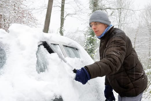 Young man removes the snow from his vehicle