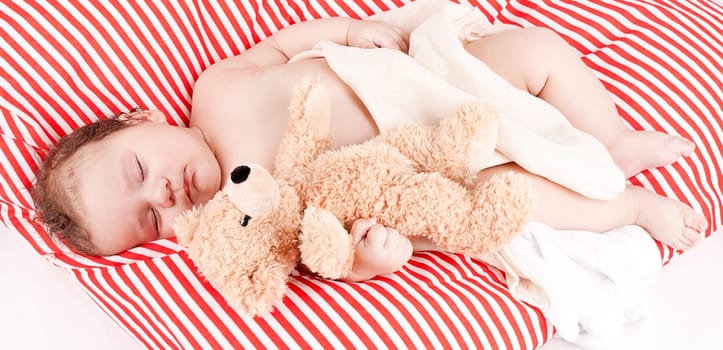 Little cute baby toddler newborn sleeps on a blanket with teddy bear in his arms
