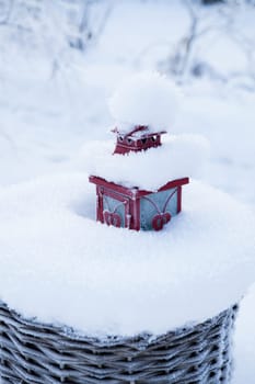 Red lantern resting in snow filled wicker basket outdoors on winter day