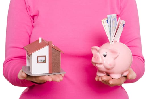 House and pink piggy bank with banknotes on a female hand