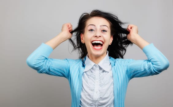 Portrait of an excited young girl standing with raised hands against grey background