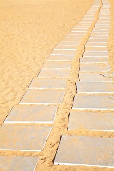 Generic Vertical take of stone flags laid to form a path from a parking lot to a beach over the hot mid day sand
