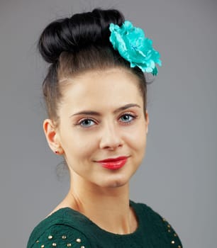 Portrait of a beautiful young woman with a flower in her hair isolated on grey