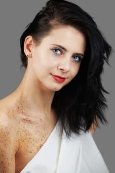 Gorgeous young woman with freckles isolated on grey with a white sheet to cover herself.