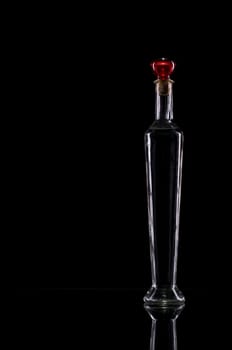 Studio shot of a long narrow decorative bottle with red cap against black background