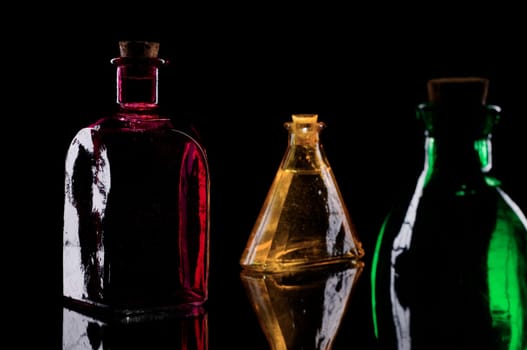 Studio close-up of three different decorative bottles against a black background in sidelight  red square bottle  yellow triangular bottle,green round bottle
