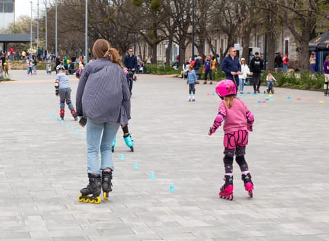 Ukraine. Kyiv. 23.04.2023. children, teenagers playing roller skates with friends outdoors. lot of children, kids go rollerblading, learn roller-skating with an adult instructor, having break in shade