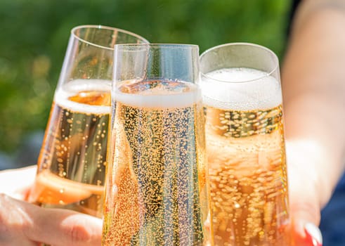 aesthetics glass at a picnic. sparkling champagne glasses. Three full glasses of champagne touch. High quality photo. friends are drinking in nature. Alcohol picnic. life style