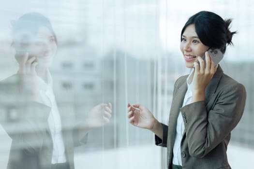 Smiling businesswoman looking through the window while talking on mobile phone in the office. Copy space.