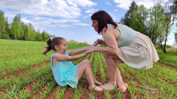 Happy mother and daughter enjoying rest, playing and fun on nature in green field. Woman and girl resting outdoors in summer or spring day