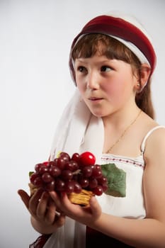 Portrait of Little girl in a stylized Tatar national costume with berries and a brush of grapes on a white background in the studio. Photo shoot of funny young teenager who is not a professional model