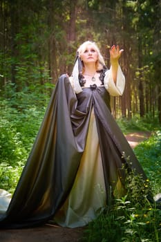 Adult mature woman 40-60 in a green long fairy dress in forest. Photo shoot in style of dryad and queen of nature. Fairy in beautiful green summer forest. Concept of caring for nature