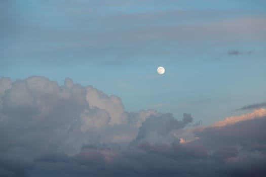 Horizontal shot cumulus clouds float across the evening sky with a full moon on a warm spring evening. Concept summer mood and good weather. Copyspace.