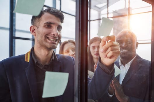 Creative business team looking at sticky notes on glass window