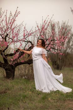 Woman peach blossom. Happy woman in white dress walking in the garden of blossoming peach trees in spring.