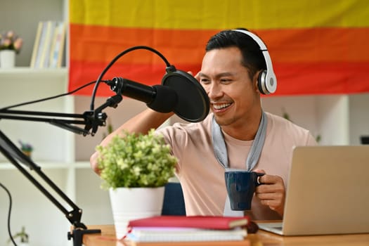 Smiling gay man radio host in headphone talking through microphone for recording conversation for channel.