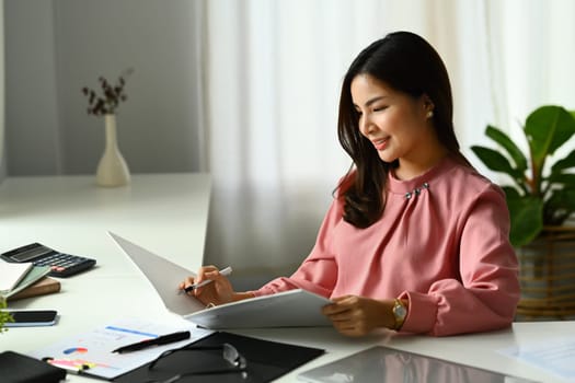 Beautiful asian female accountant checking report, financial data or bookkeeping in office.