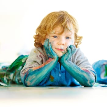 Messy, portrait and a child in paint after art in class, school or education on the floor. Happy, relax and a boy, kid or kindergarten student covered in color after painting, creativity or playing.