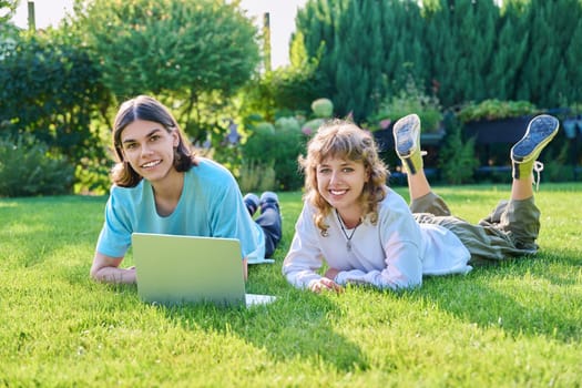 Two teenage friends of students lying on grass with laptop, in backyard, guy and girl 16, 17 years old study together. Friendship, youth, technology, high school, college, lifestyle concept