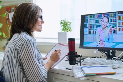 Mature woman talking online with teenage girl using video call on computer, home interior. Virtual meeting, therapy session with psychologist. Chat conference technology psychology education learning