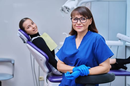 Portrait of smiling female dentist looking at camera with young teenage girl patient sitting in dental chair. Visit to dentist examination treatment. Dentistry hygiene dental teeth health care concept