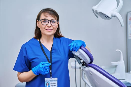 Portrait of smiling female doctor dentist in office. Confident middle aged woman looking at camera near dental chair. Dentistry, examination, occupation, teeth health care concept