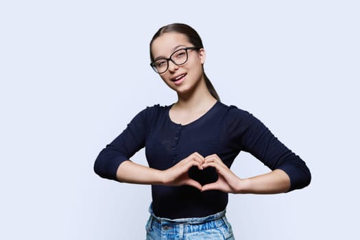 Young smiling female showing heart gesture with fingers, happy female showing love, white studio background. Body language, signs symbols, love, emotions, romance youth concept