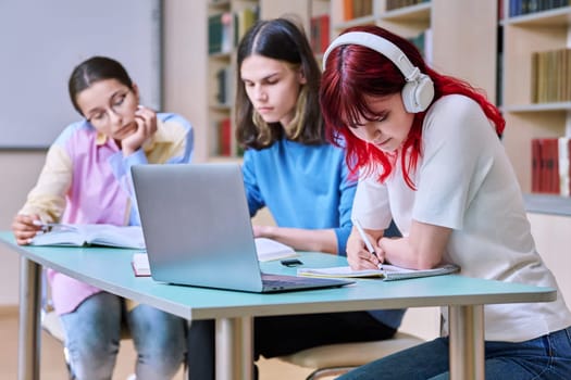 Group of teenage students study at their desks in library class. Teen students writing in notebooks using books laptop. Education, knowledge, high school, college concept