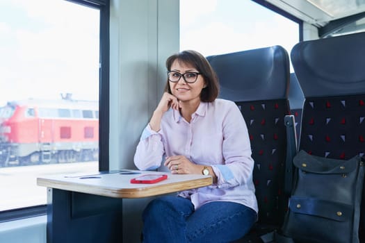 Woman sitting inside electric train, middle age female passenger smiling looking at camera. Transport, electric transport, railroad, people concept