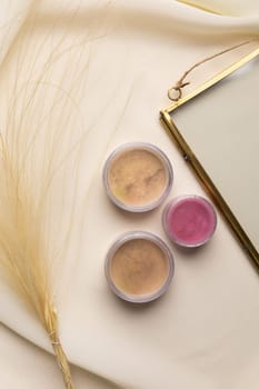 Cosmetics facial powder and blush for cheeks on natural background with dried flowers. Makeup accessories top view.